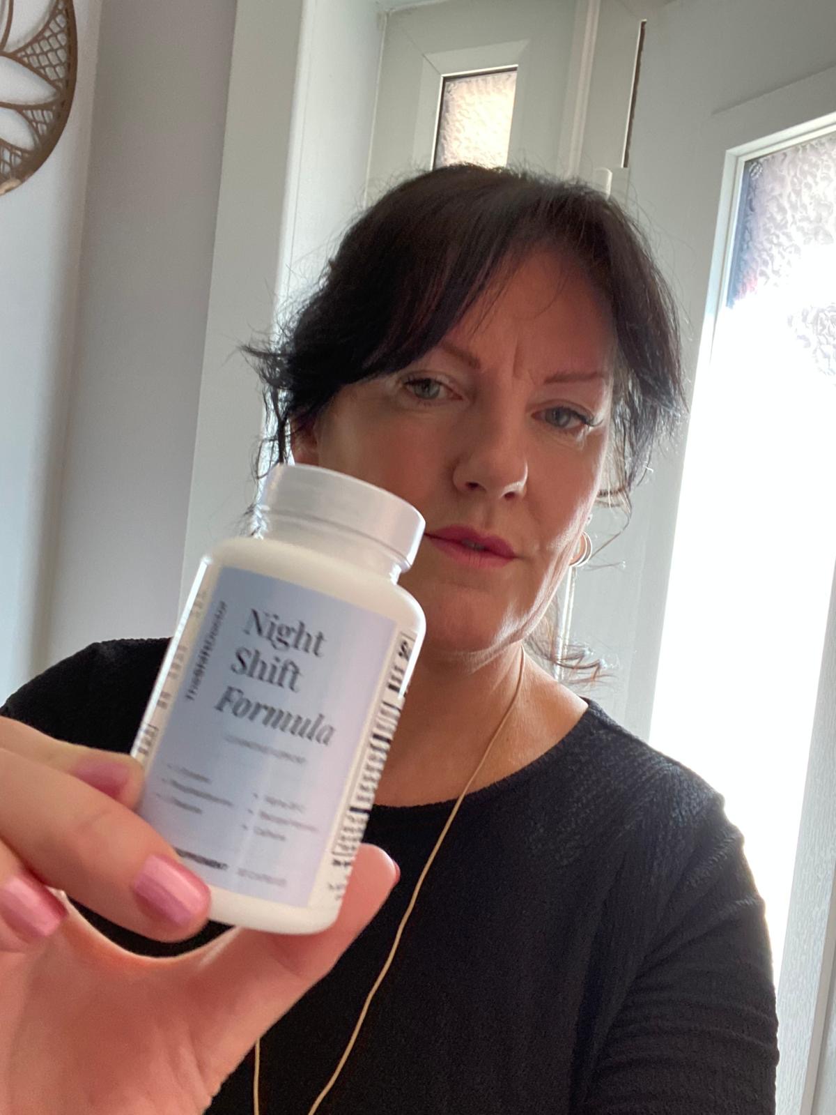 Sarah in her ICU nurse work uniform holding a bottle of Night Shift Formula cognitive support supplement